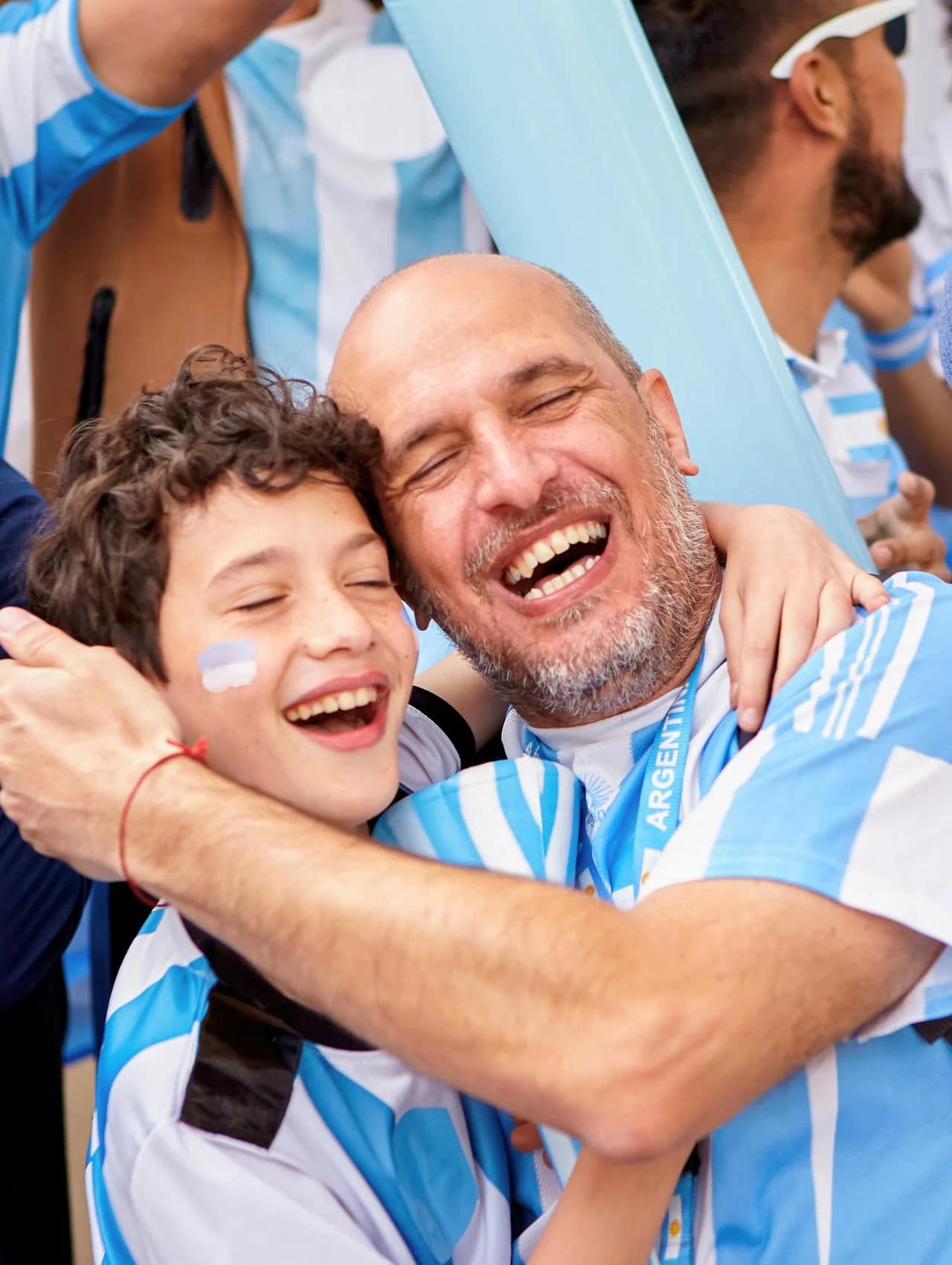 Padre e hijo abrazados y riendo en un estadio de fútbol con camisetas de Argentina, la mejor idea de regalos para el día del padre