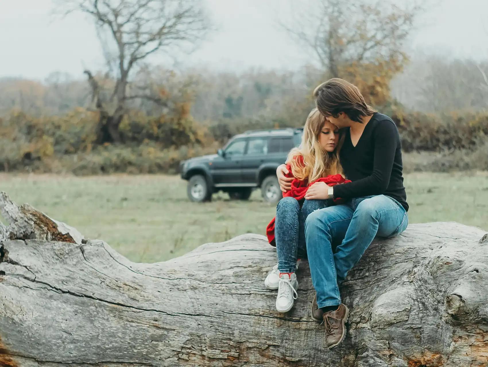Pareja sentada en un tronco al aire libre abrazándose con ternura – como resolver peleas de pareja