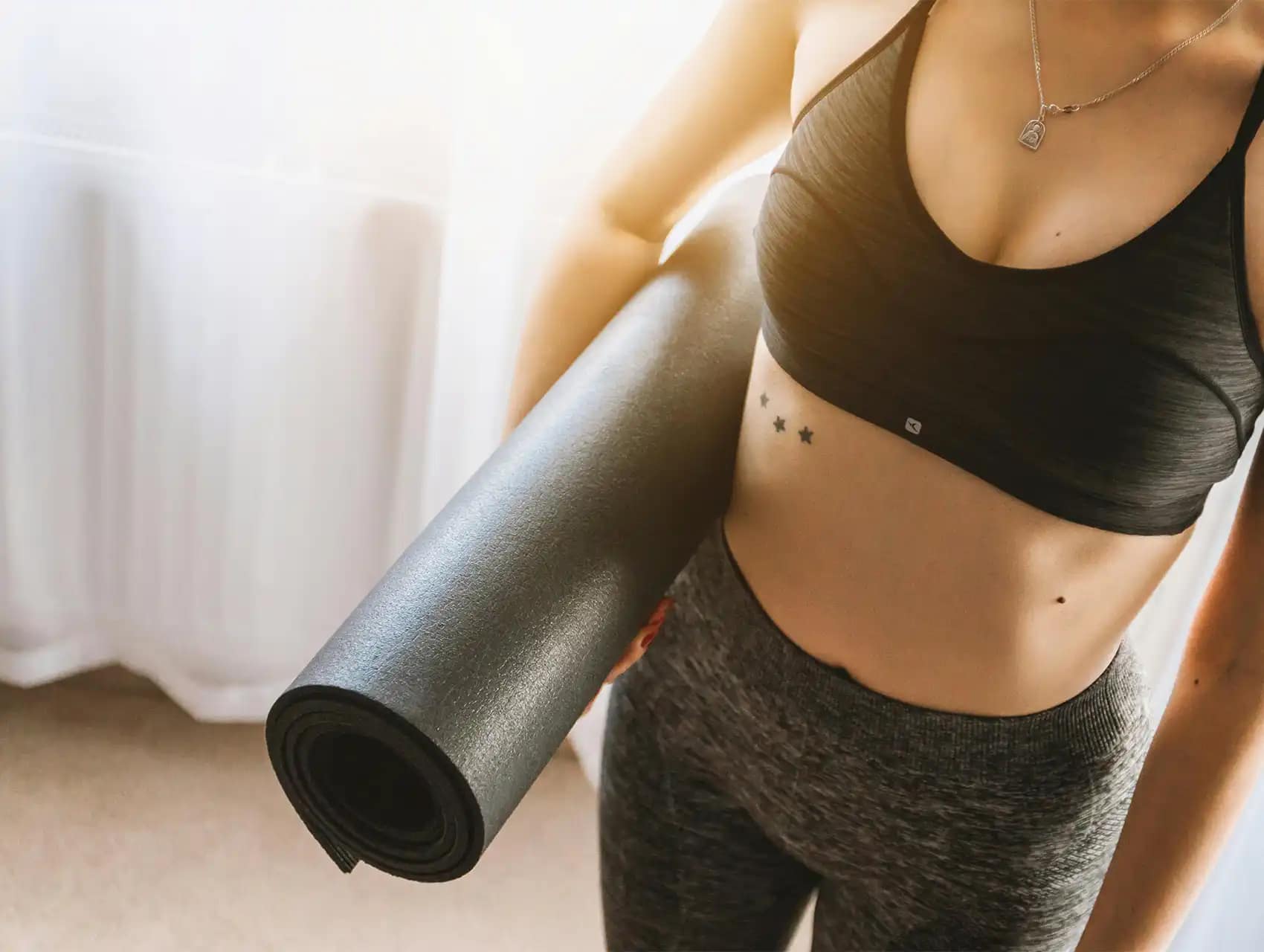 Fit woman holding a yoga mat while wearing workout clothes, illustrating healthy lifestyle and the question: do waist trainers work.