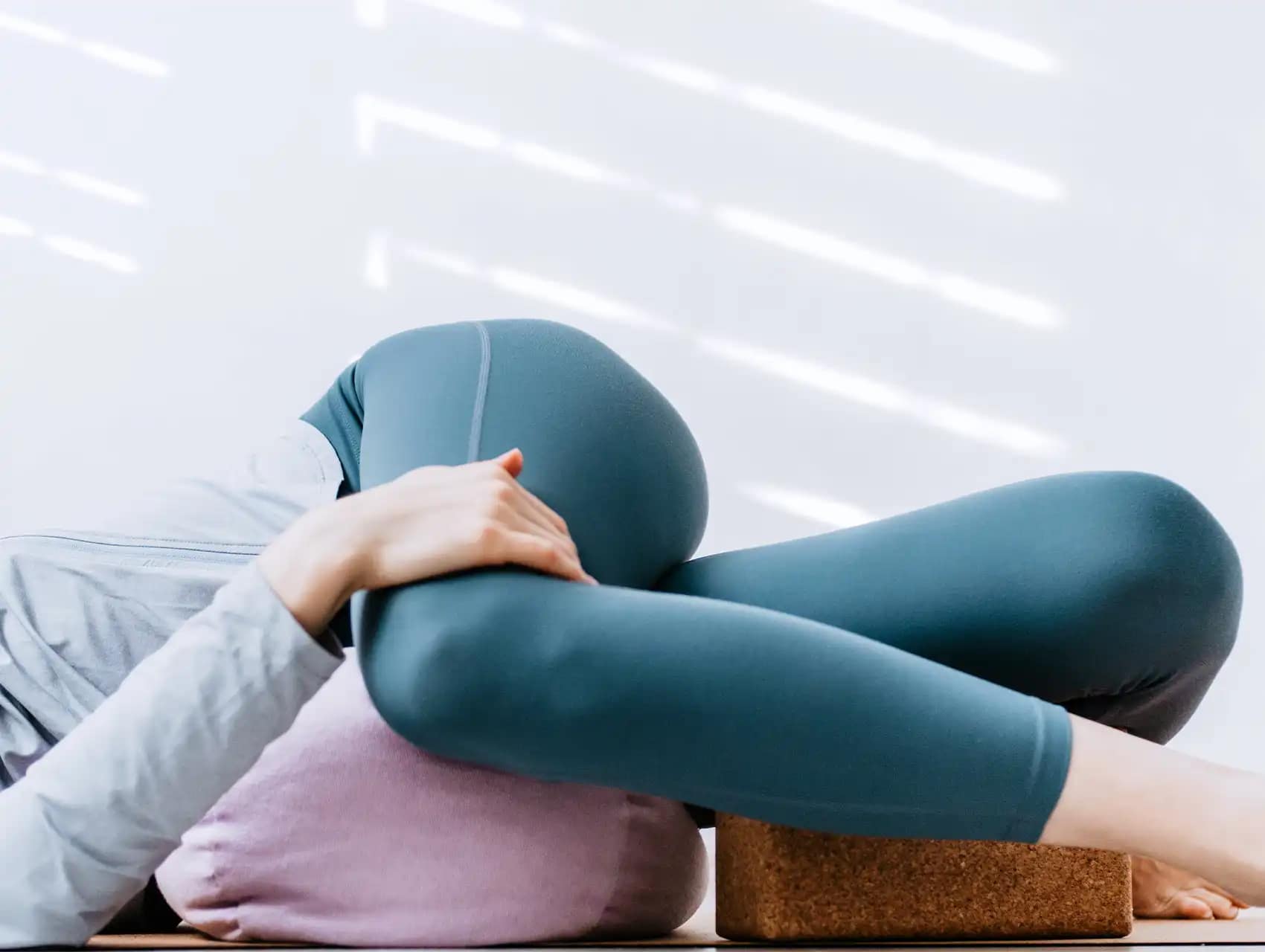 Woman lying on pink bolster in supported yoga twist pose with bolsters
Woman lying on pink bolster in supported yoga twist pose with bolsters