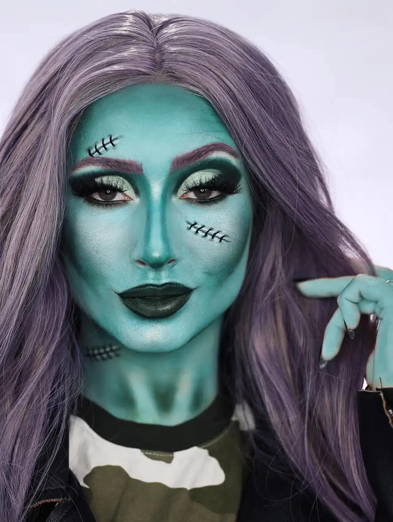 Zombie halloween makeup looks with green face paint, stitches, and purple wig.