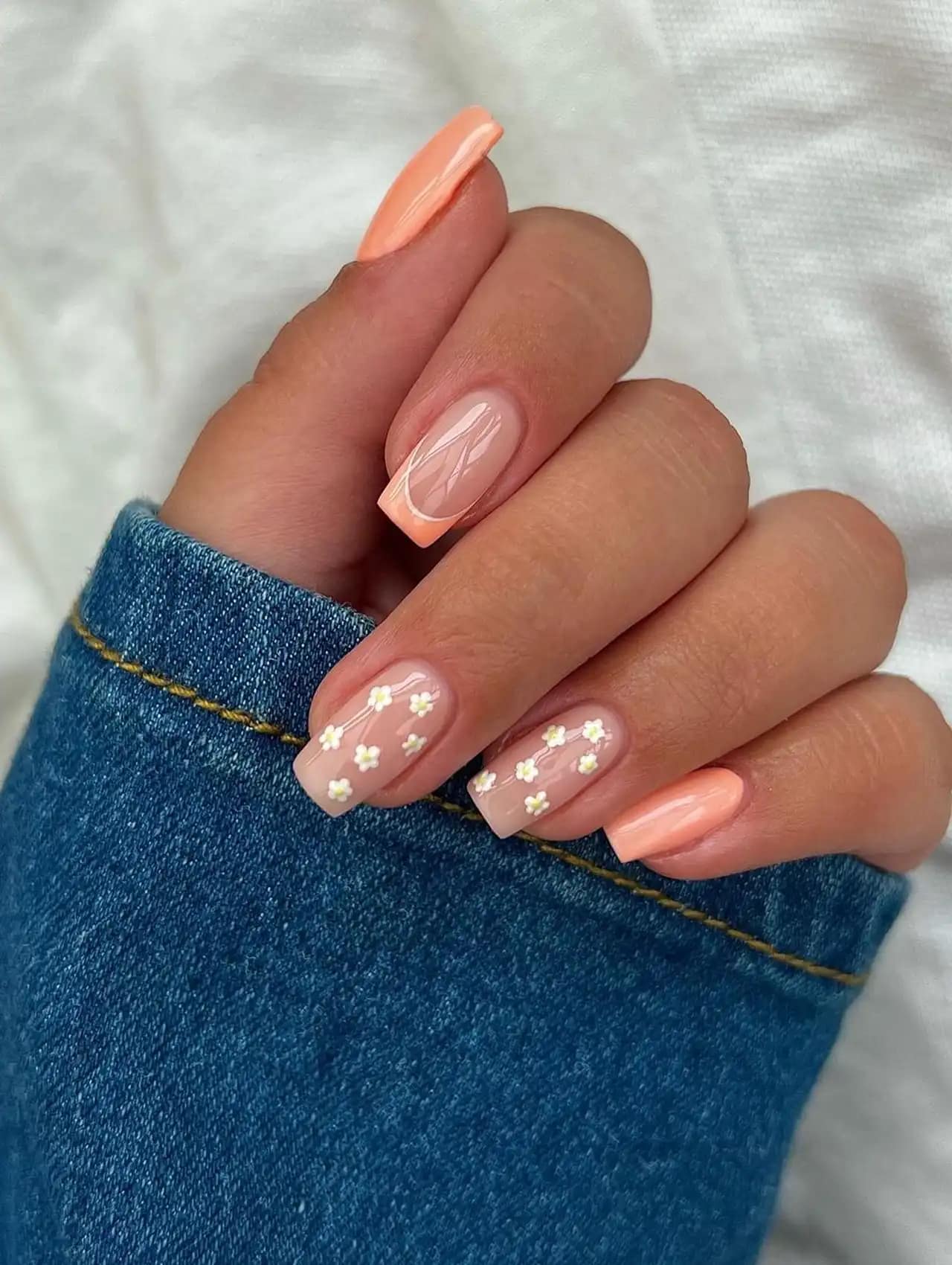 Square nails with peach polish, French tips, and delicate white floral accents, nail art design 2025.