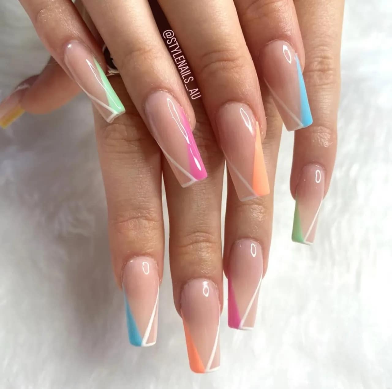 Diseño de uñas geométrico con líneas blancas y bloques de color sobre base nude.