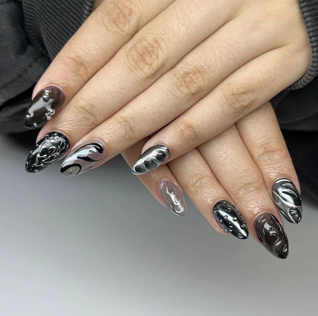 Diseño de uñas negro y plateado con efecto tridimensional y detalles modernos.