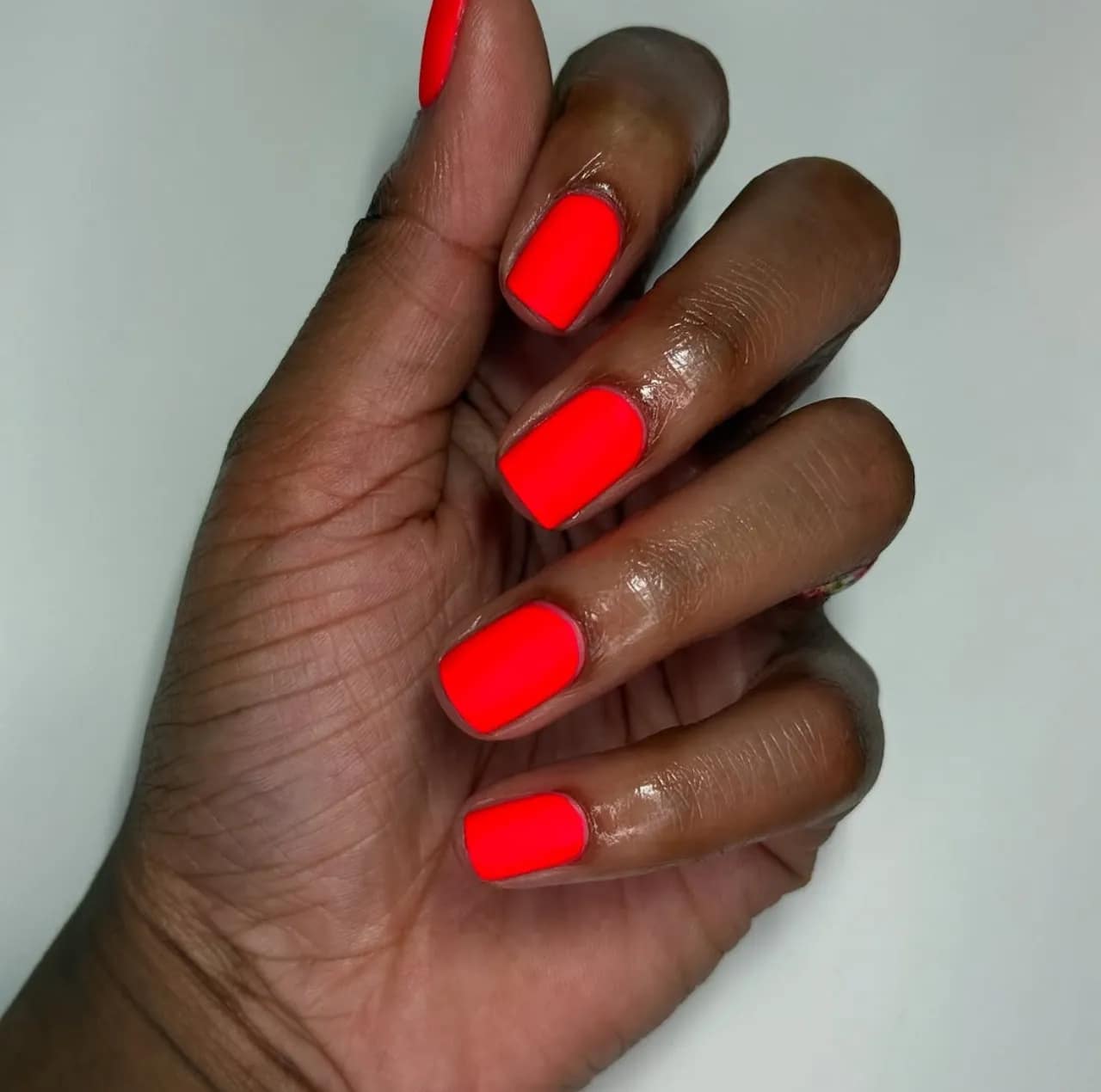 Diseño de uñas en tono neón rojo vibrante sobre uñas cortas.