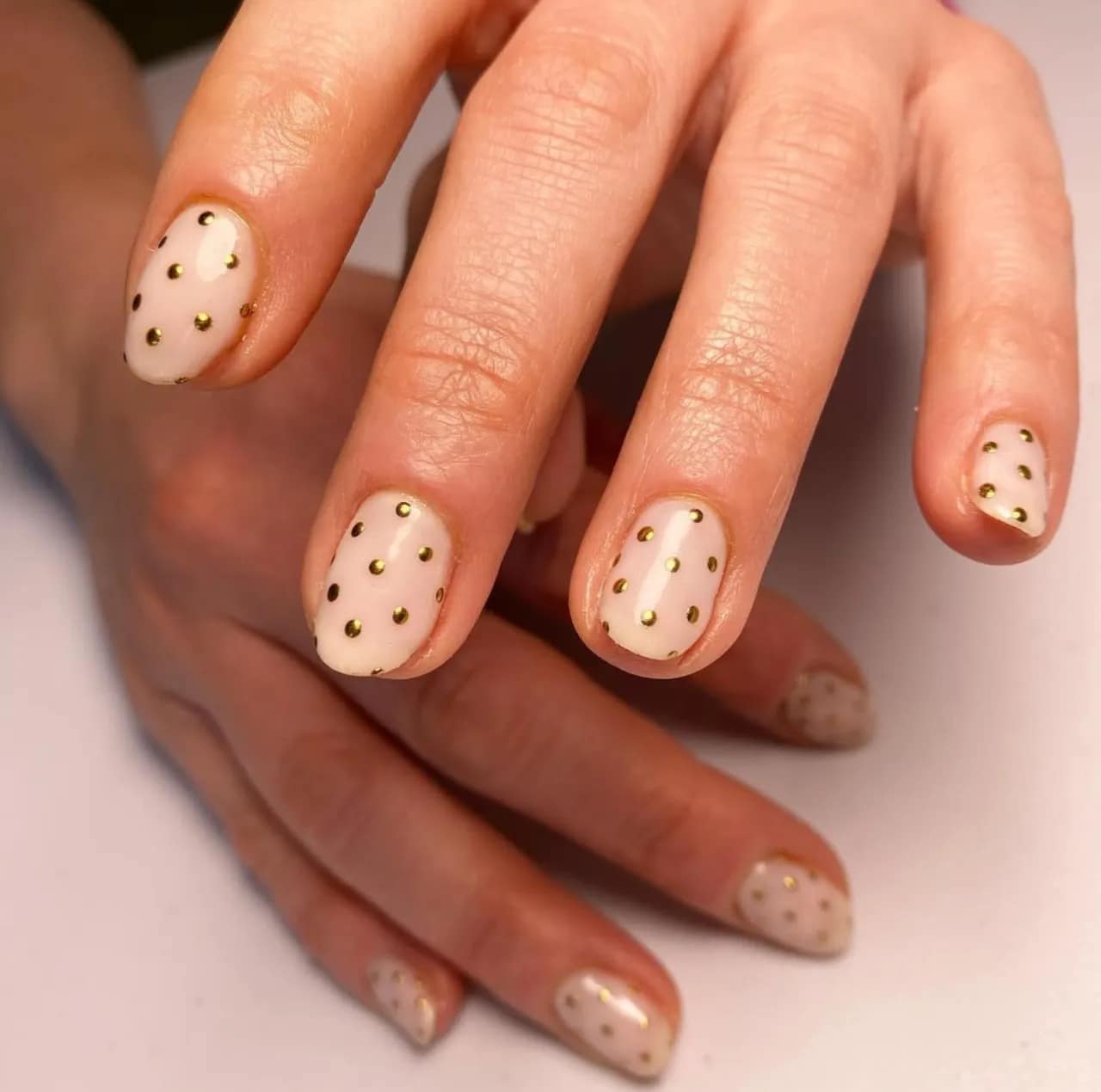 Diseño de uñas con piedras y tachuelas doradas sobre base nude.