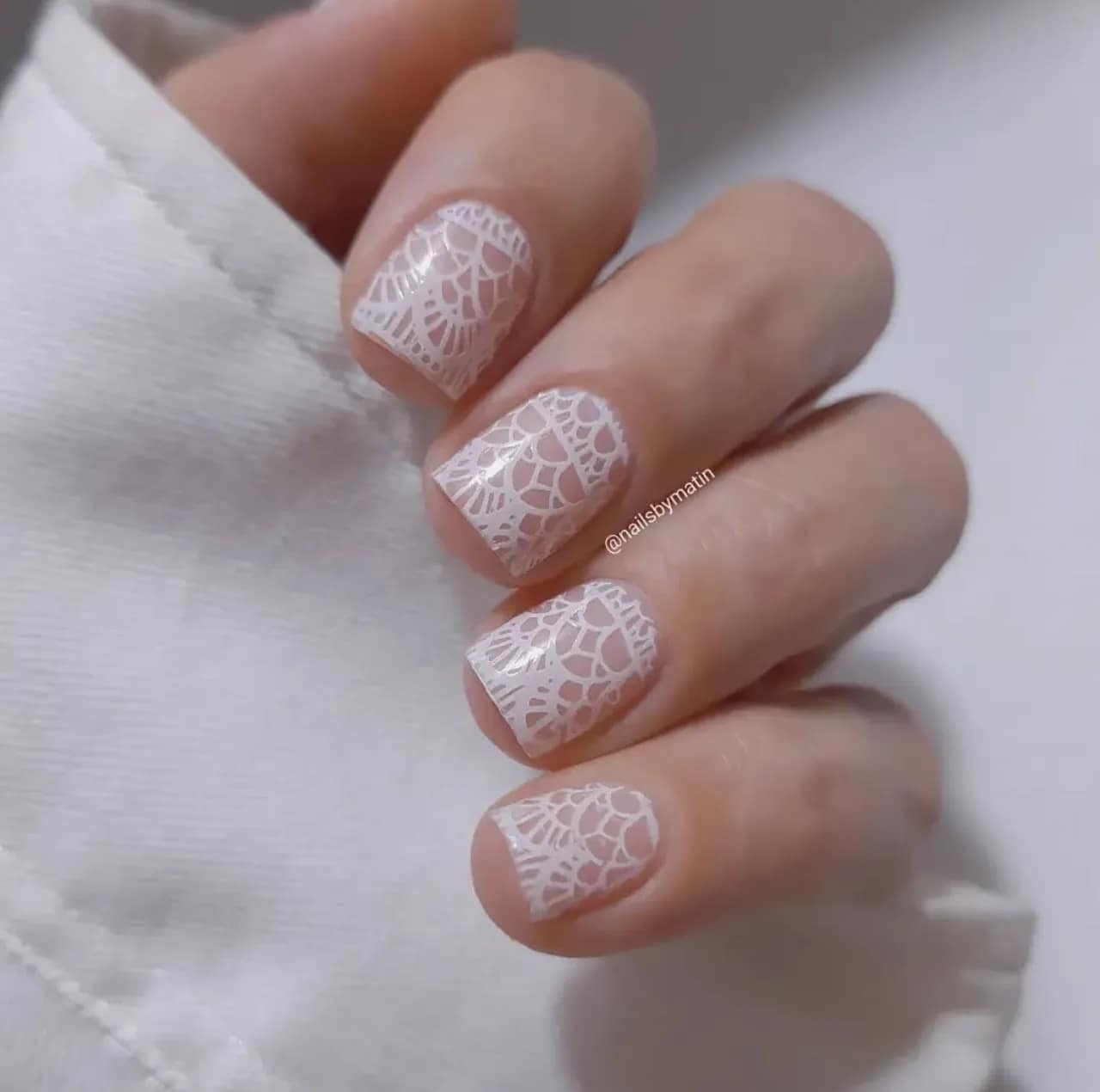 Diseño de uñas de encaje blanco sobre fondo nude en uñas cortas.