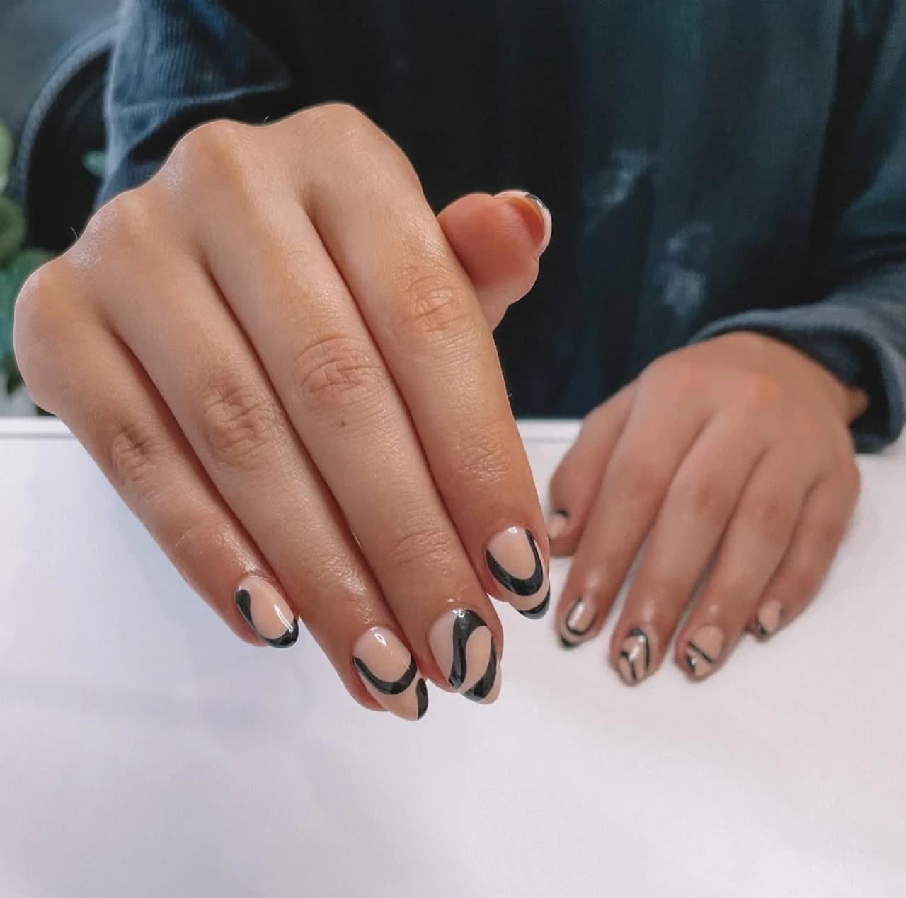 Diseños de uñas acrílicas abstractas con patrón negro sobre base nude.