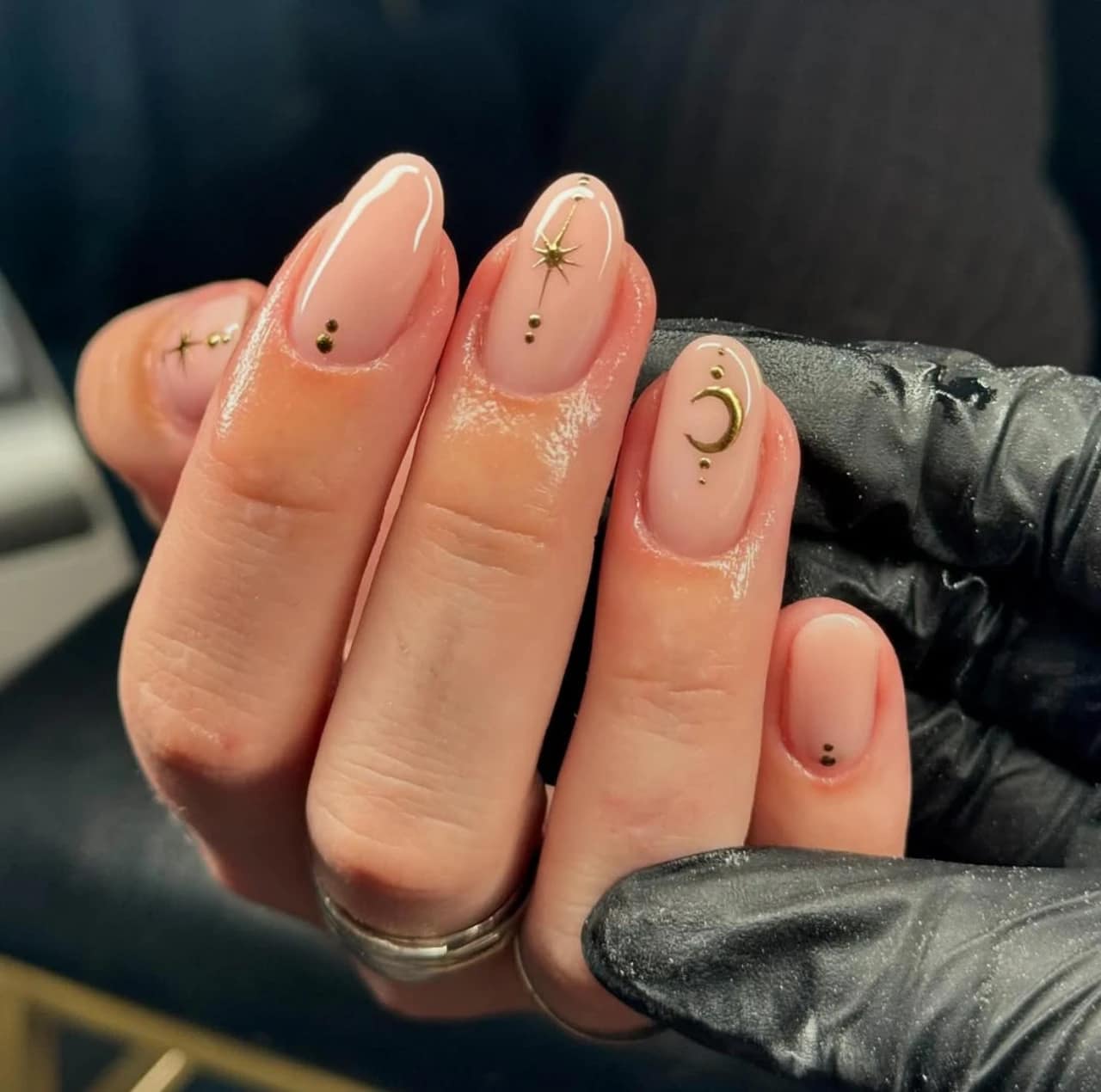 Diseños de uñas acrílicas con detalles dorados de luna, estrellas y puntos sobre base nude.