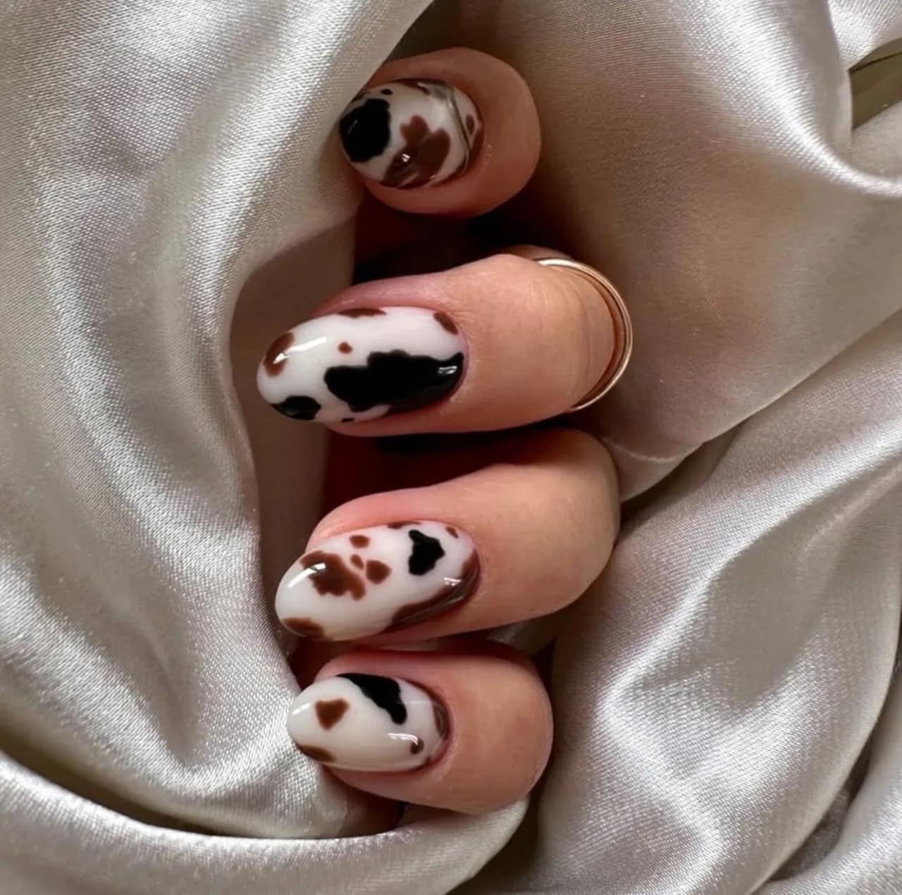 Diseños de uñas acrílicas de vaca con manchas en tonos marrón y negro sobre fondo blanco.
