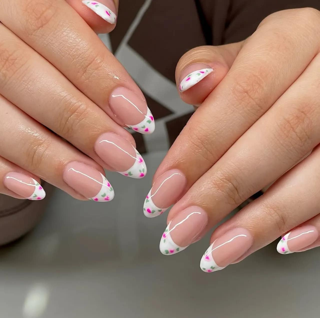 Diseños de uñas acrílicas francesas con flores en tonos rosa y verde sobre base blanca.