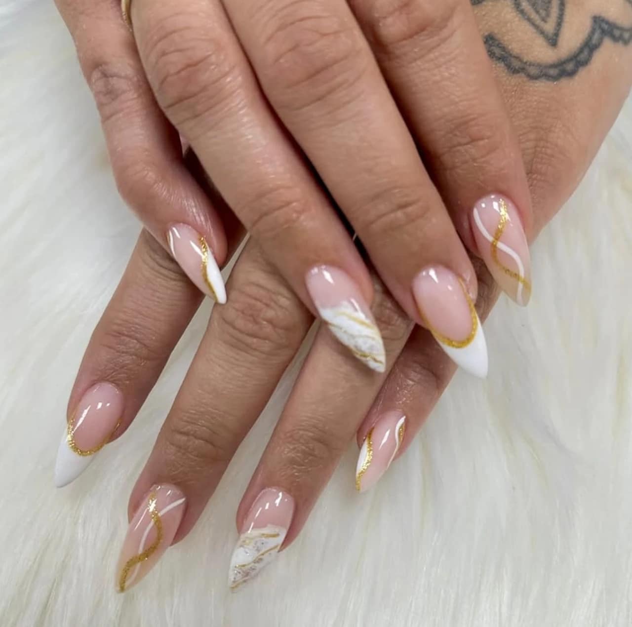Diseños de uñas acrílicas abstractas con detalles en dorado, blanco y nude.