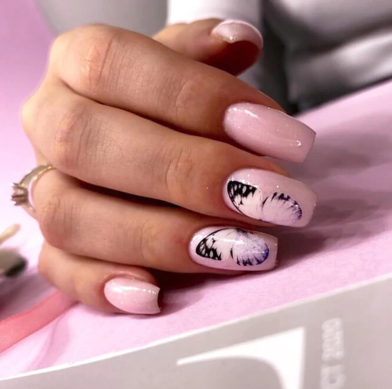 Diseños de uñas acrílicas rosadas con mariposa decorativa en estilo delicado y femenino.