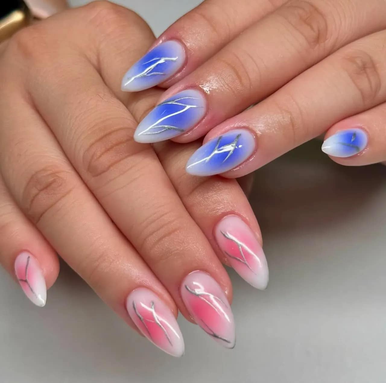 Efecto aura en uñas con degradado azul y rojo decorado con líneas metálicas.