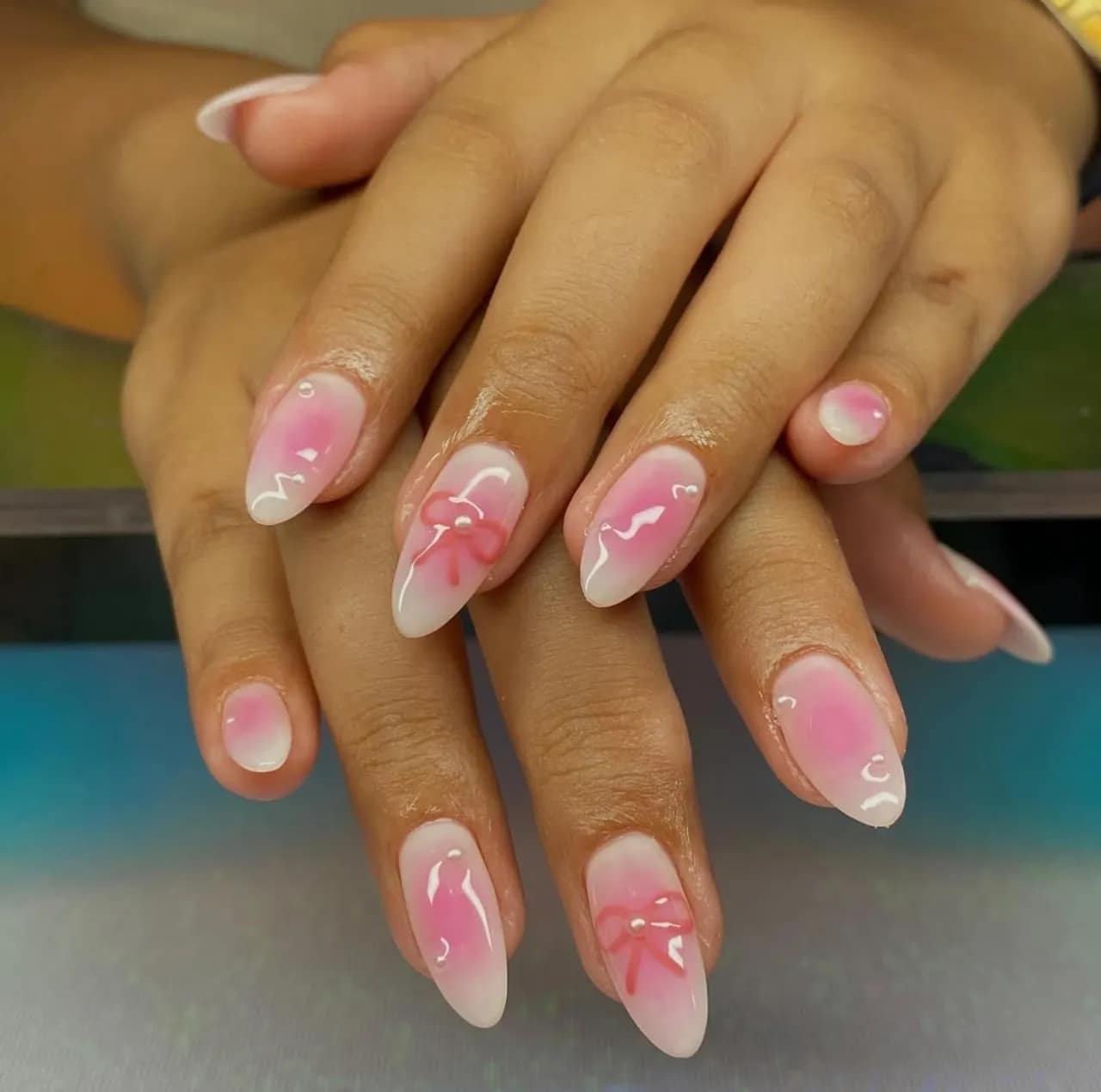 Efecto aura en uñas coquette con lazo rosa, detalles brillantes y acabado romántico.