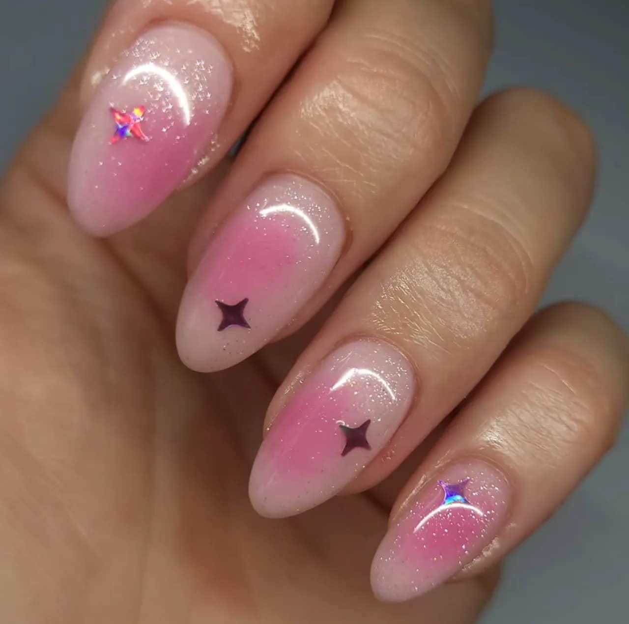 Efecto aura en uñas con glitter rosado y decoraciones de estrellas holográficas.