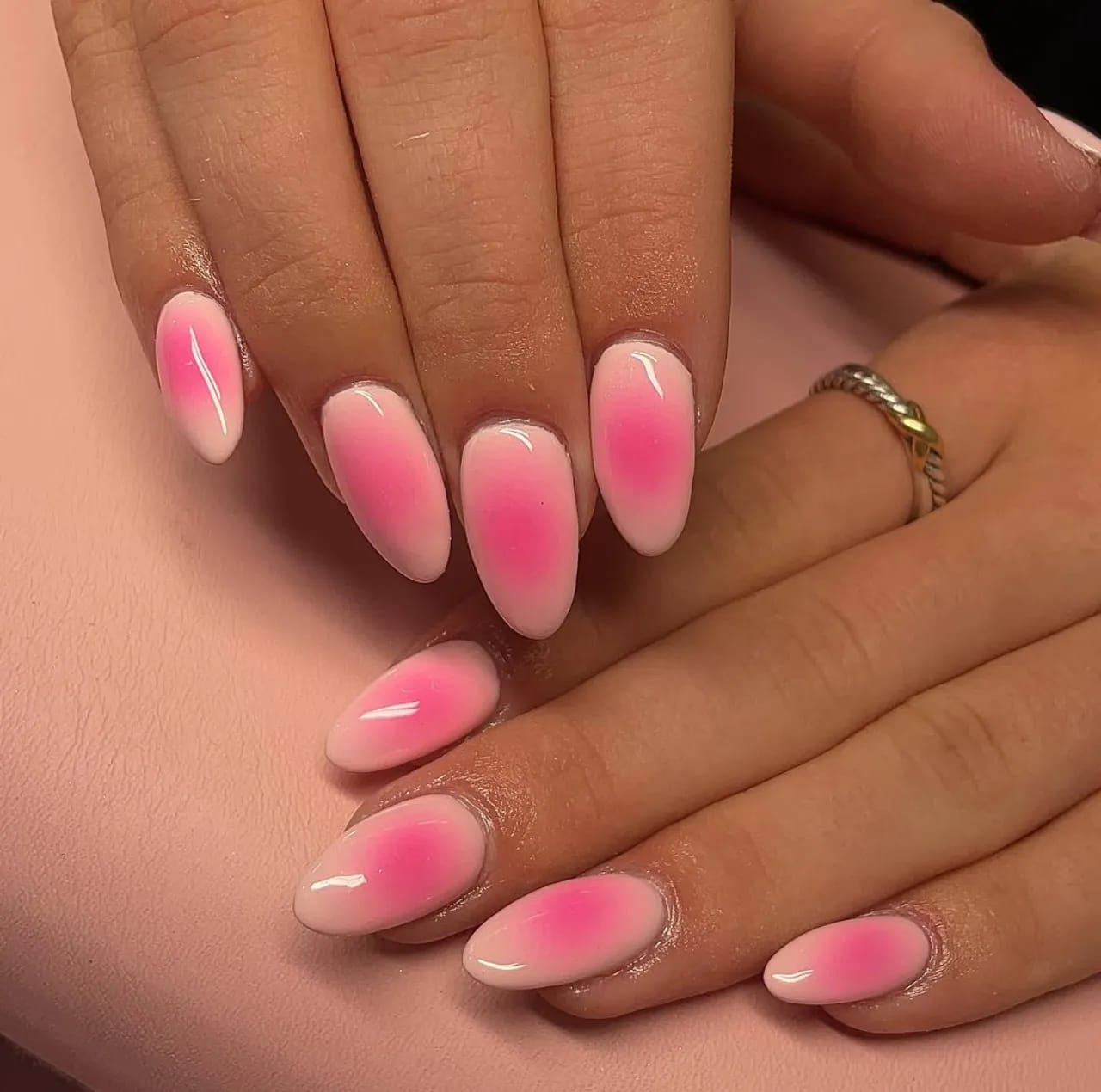 Efecto aura en uñas con degradado rosado sobre base clara y acabado brillante.