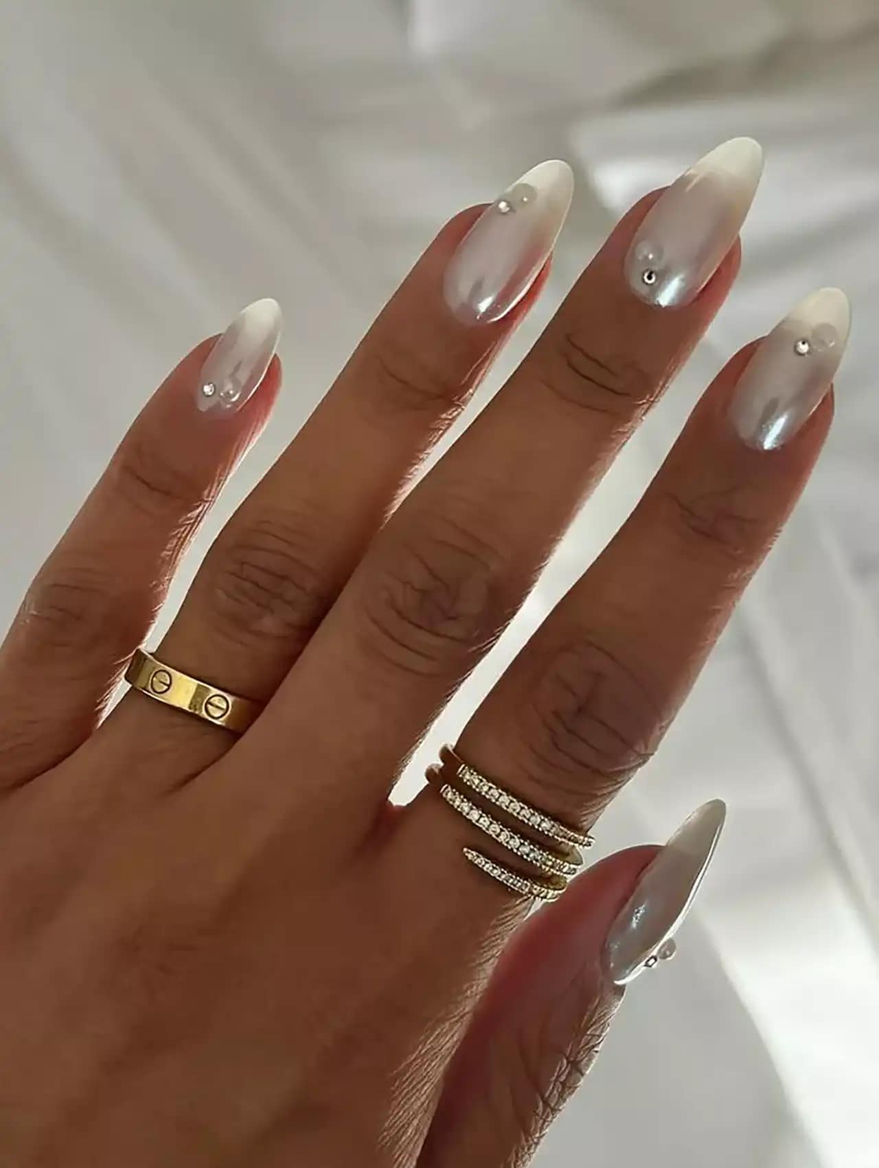 White ombré nail polish with small silver studs on almond nails.
