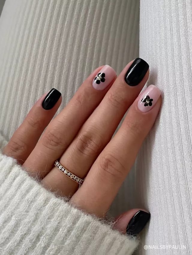 A chic black and nude nail design featuring glossy black polish and delicate floral accents.