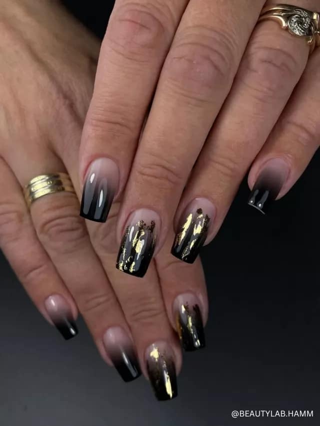 A luxurious black ombre nail design with gold foil accents and a glossy finish.