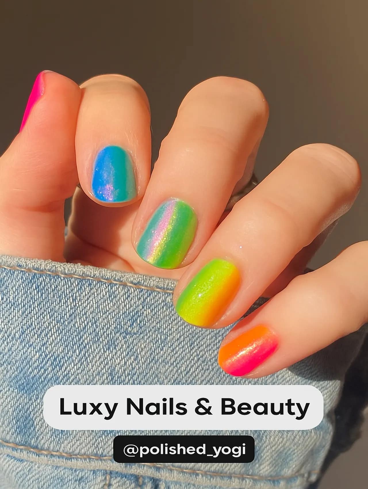Close-up of a hand with short iridescent rainbow nails from Luxy Nails & Beauty, featuring a bright, shimmering gradient.