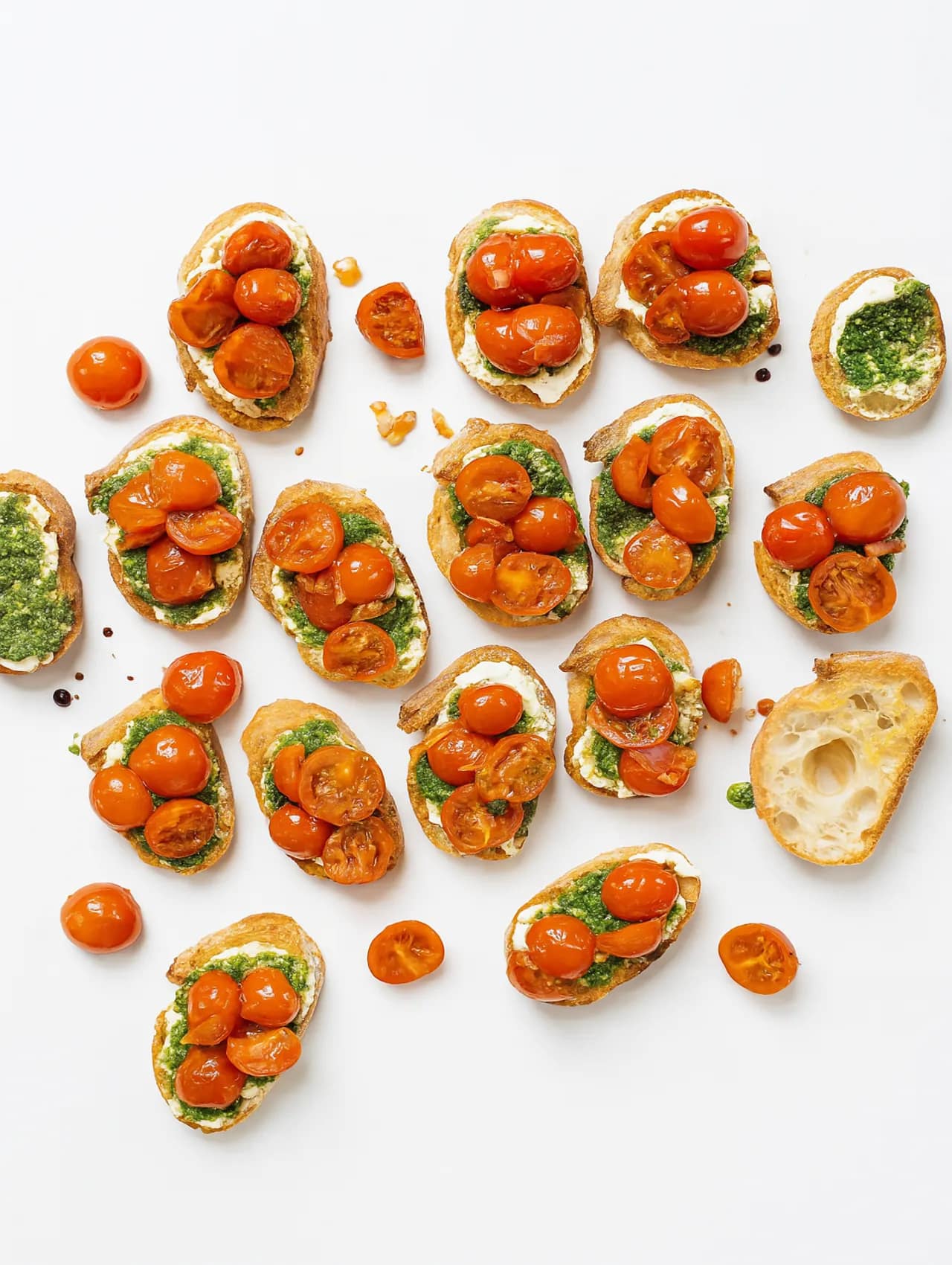 Bruschettas con pesto y tomate cherry servidas sobre pan crujiente en fondo blanco, ideales para eventos o reuniones