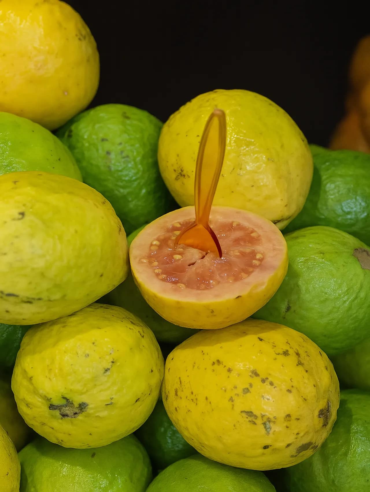 Guayabas maduras y verdes apiladas, con una guayaba cortada a la mitad mostrando su pulpa rosa, utilizada para hacer bocadillo colombiano